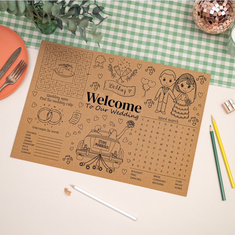 Wedding Activity Mat which says welcome to our wedding. The Mat is Kraft Brown and has wedding themed puzzles, colouring and activities. The Placemat is against a checkered table cloth.