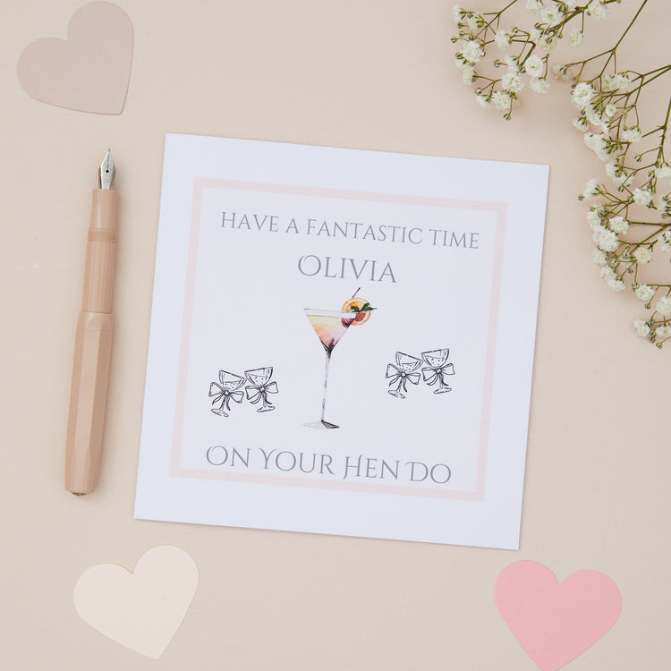 Bridal Shower Hen Do Card which has the text "have a fantastic time on your hen do". There is a cocktail glass with a cocktail in it, with a pair of vintage glasses either side. Back ground is neutral with stationery.