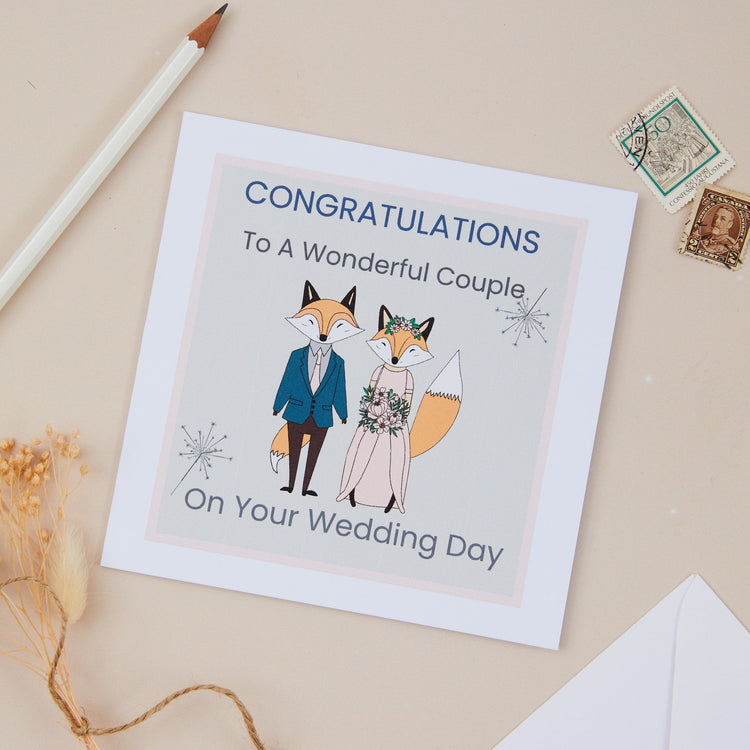 A wedding congratulations card featuring a couple on their wedding day. There are two cartoon foxes dressed in their wedding attire. The Card says congratulations to a wonderful couple on your wedding day