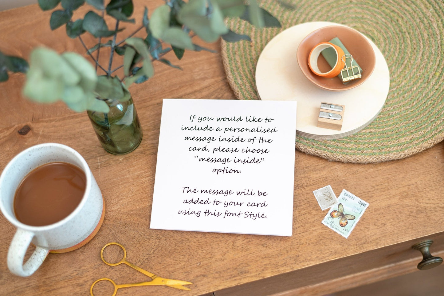 Example of the font and message that can be included in the card if a customer would like to include a personalised message. This Card with the personalised message example is on a table with green flowers, tea and stationery pieces
