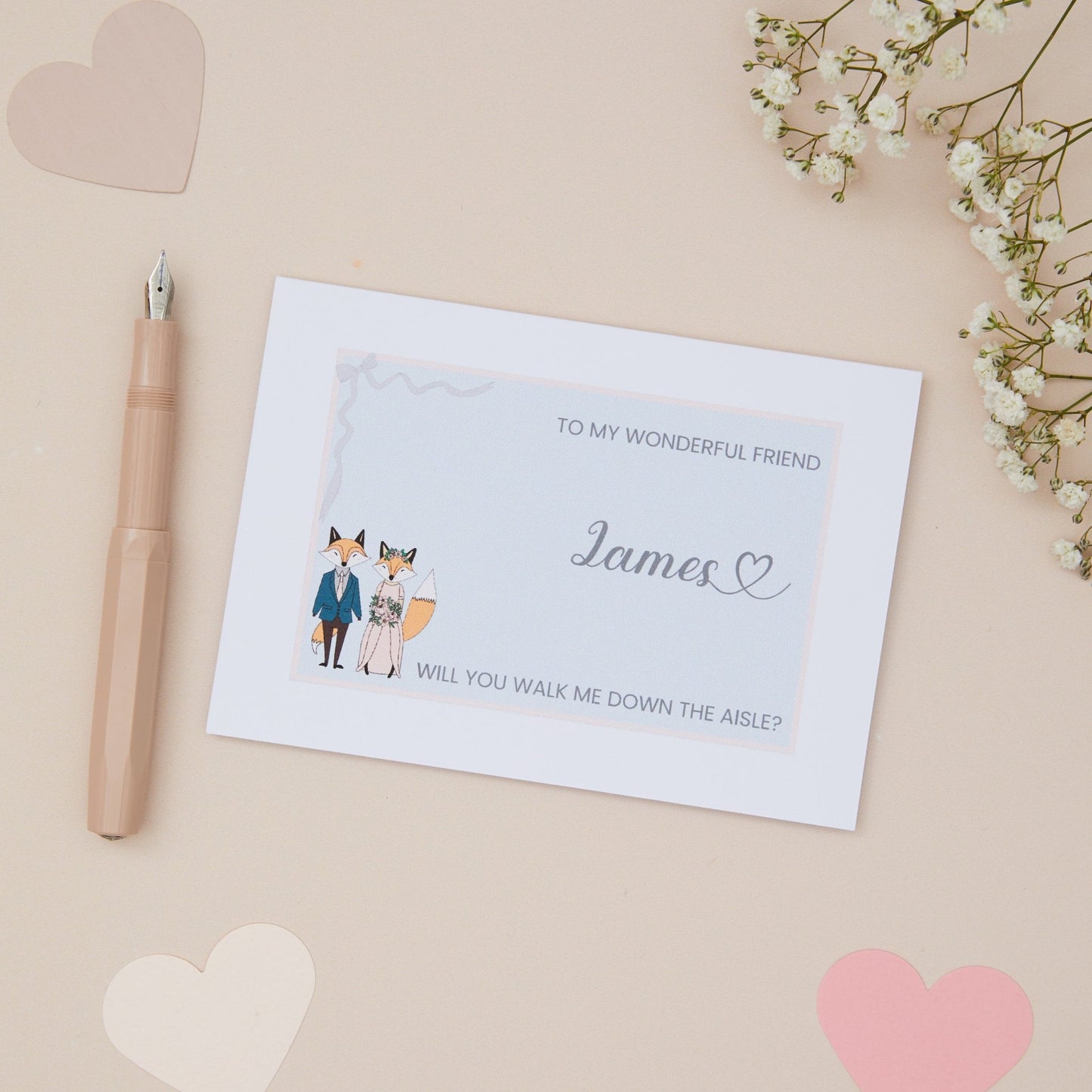Friend will you walk me down the Aisle proposal Card. A fox couple in wedding bridal attire with the label 'To my wonderful Friend, will you walk me down the aisle. The Card is set against a pale beige background with stationery items.