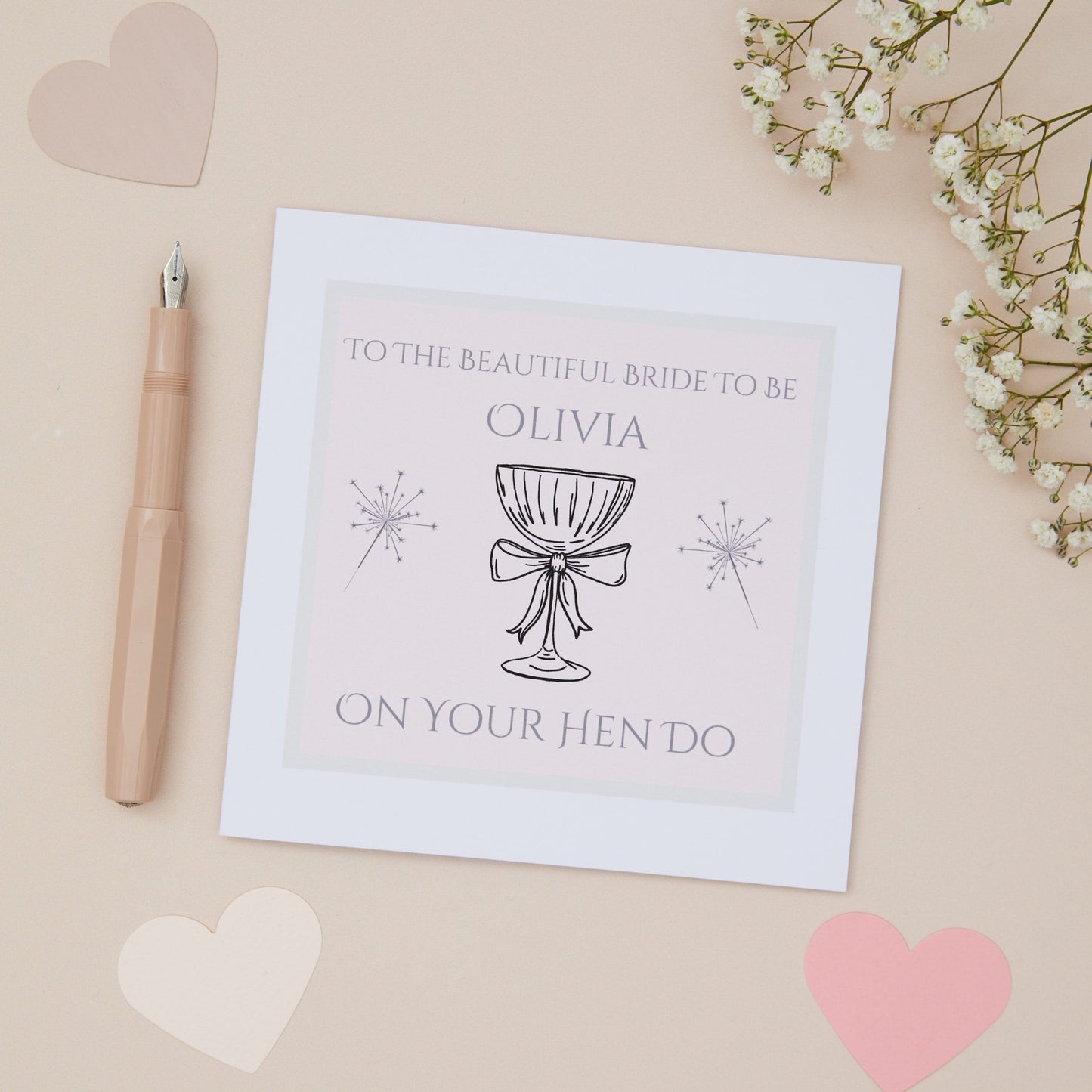 A Hen Do, bridal shower card with a Celebratory glass with a bow illustration, the text 'To the beautiful Bride to be on your Hen Do', accompanied by decorative hearts and flowers on a beige background.