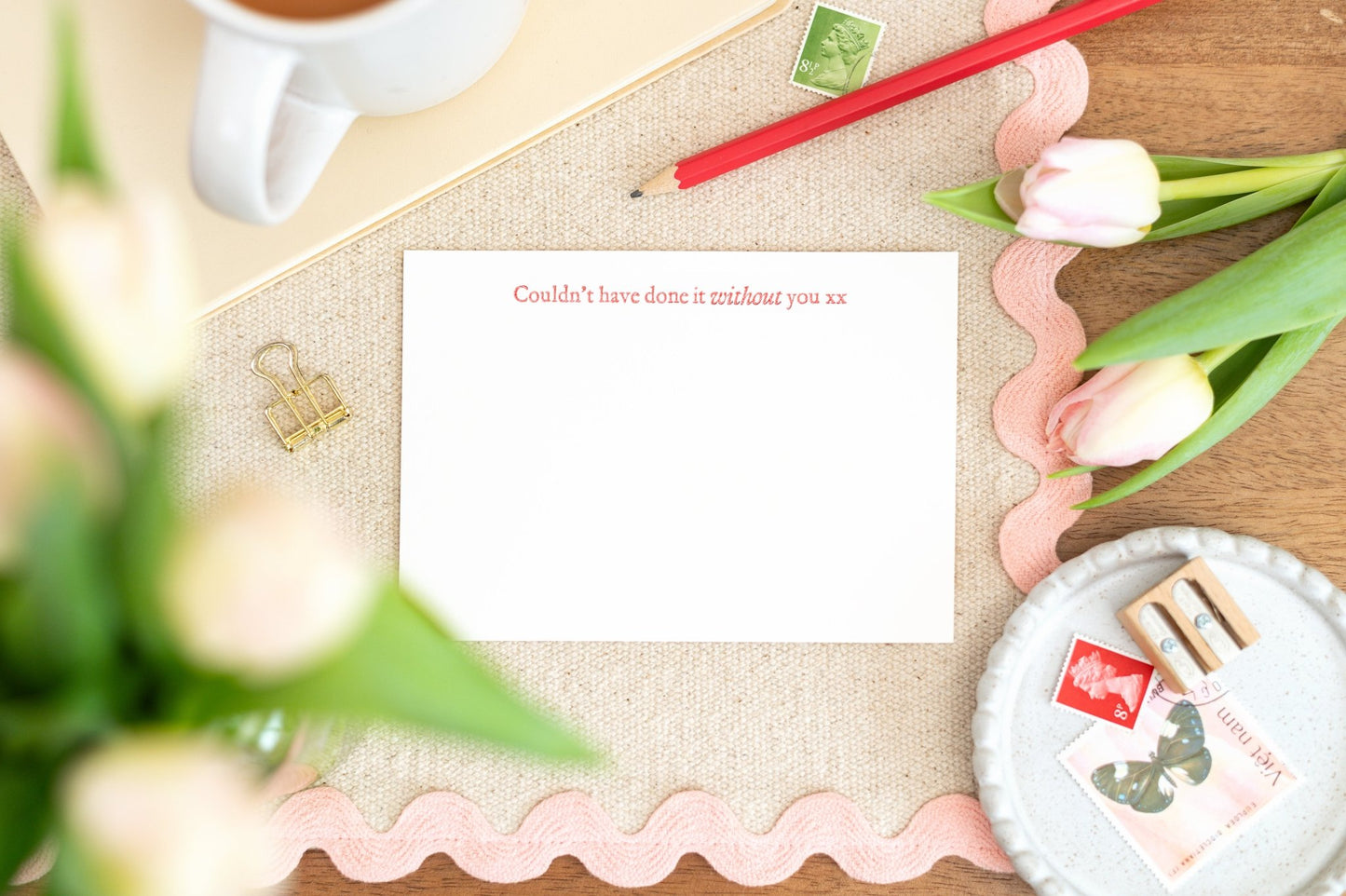 A flat letterpress notelet with 'Couldn't have done it without you' text in Red Letterpress typography surrounded by tulips, a cup, and writing utensils, indicating a message of gratitude.