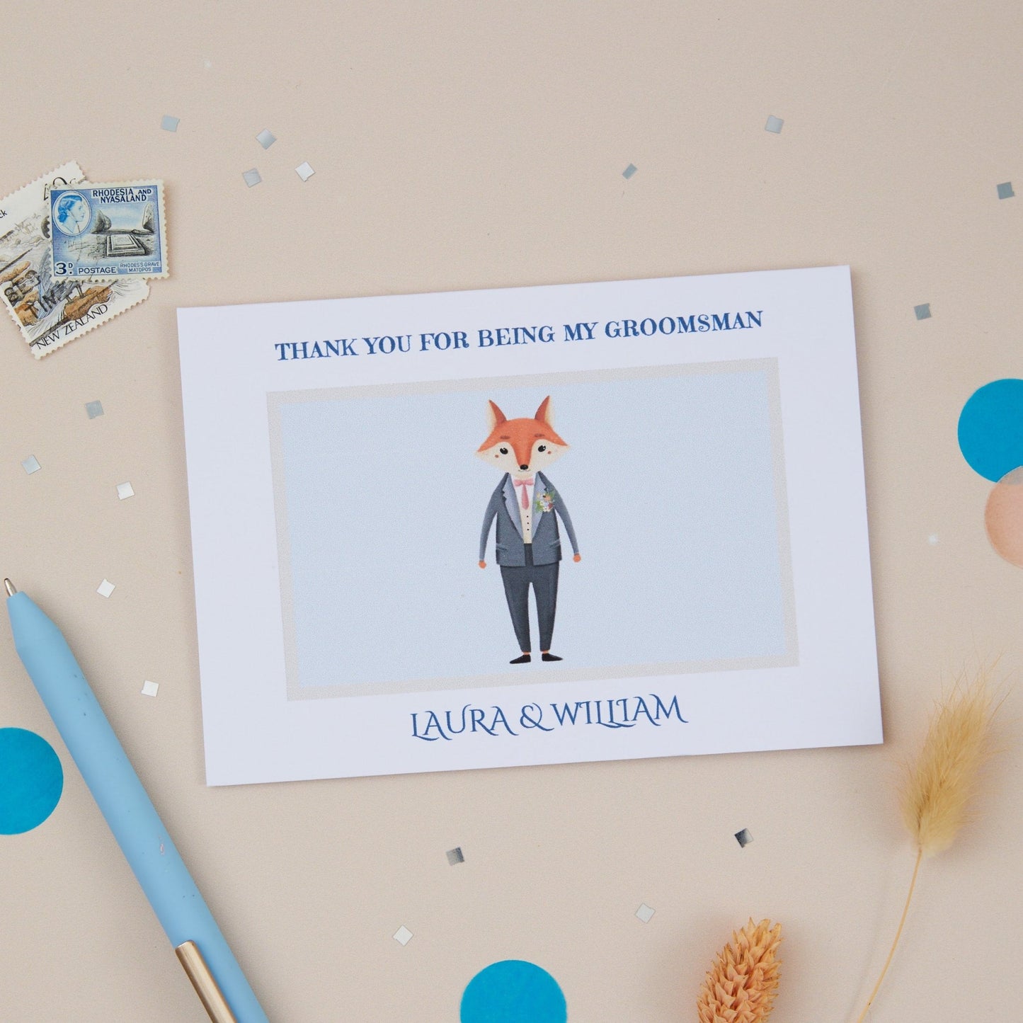 A thank you card for a groomsman with a cartoon illustration of a fox in a suit. The card is placed on a neutral background with some decorative elements, including a blue pen and vintage stamps.