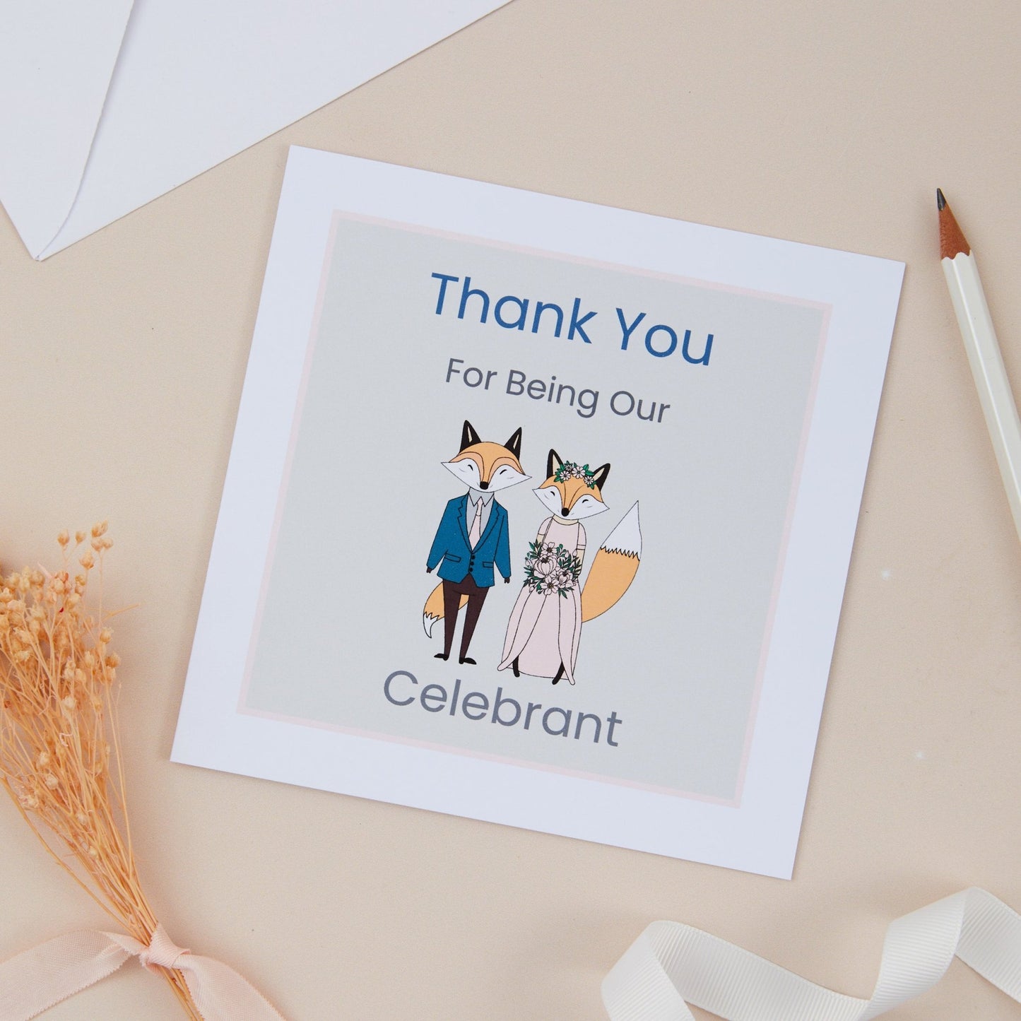 A square wedding thank you for being our Celebrant card with an illustration of a bride and groom standing close. The card is placed on a neutral background with a lined envelope, ribbon, and a pencil to the side.