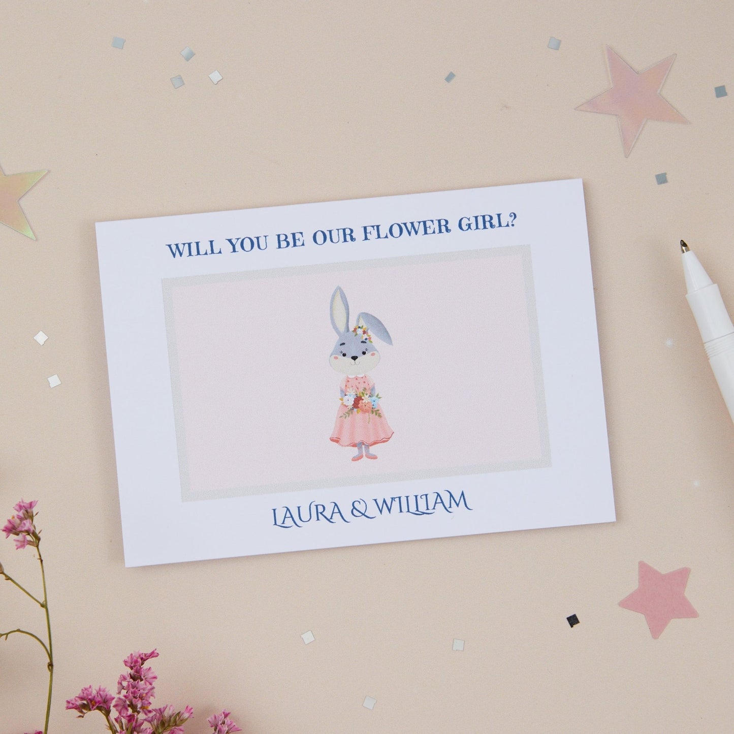 A "Will You Be Our Flower Girl?" card with a floral theme, featuring a cute rabbit and a pink dress, displayed on a neutral background with some decorative elements like stars and flowers.