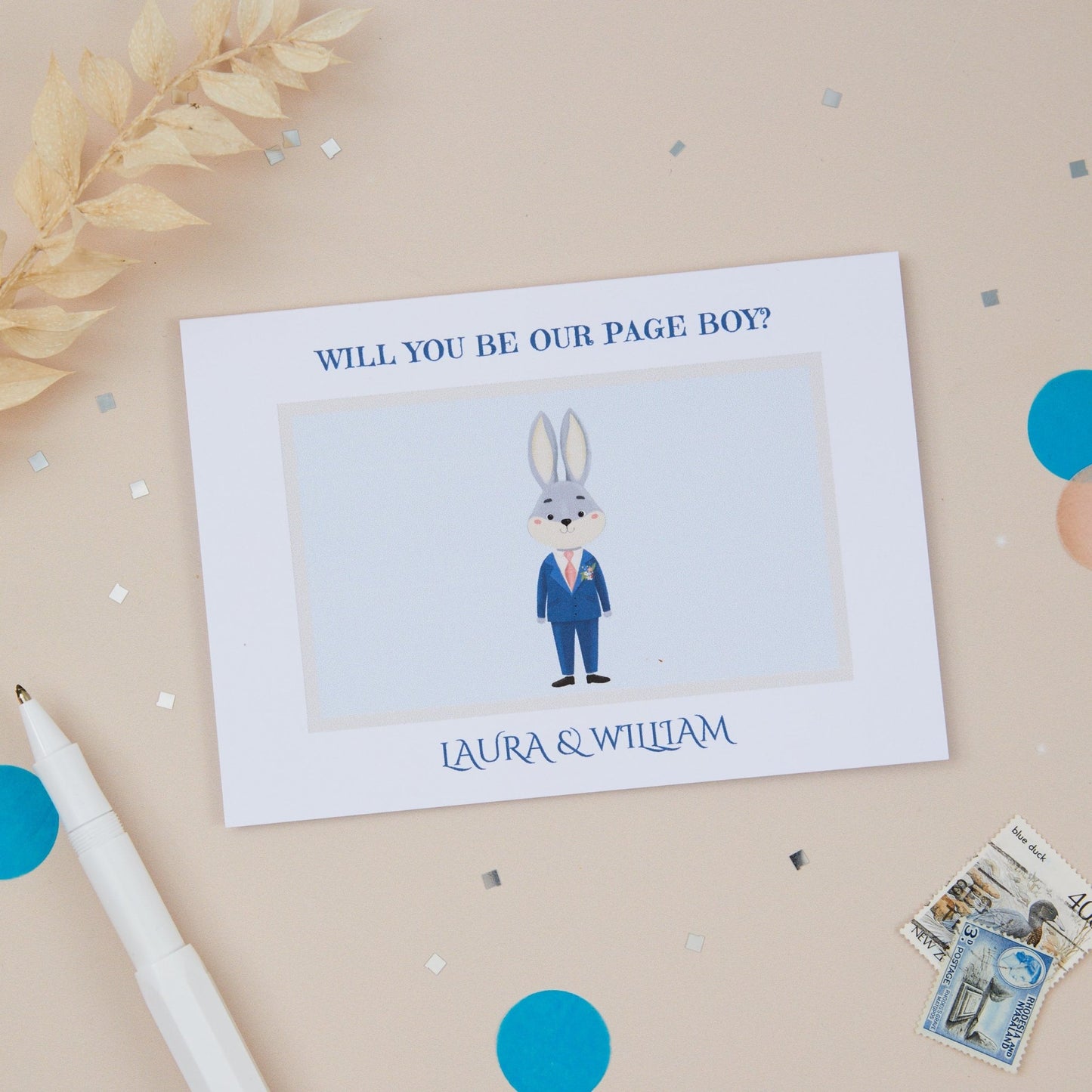 A proposer card titled 'WILL YOU BE OUR PAGE BOY' with a cartoon illustration of a bunny page boy wearing a suit. The card is placed on a neutral background with some decorative elements like a pen, coins, and a watch.