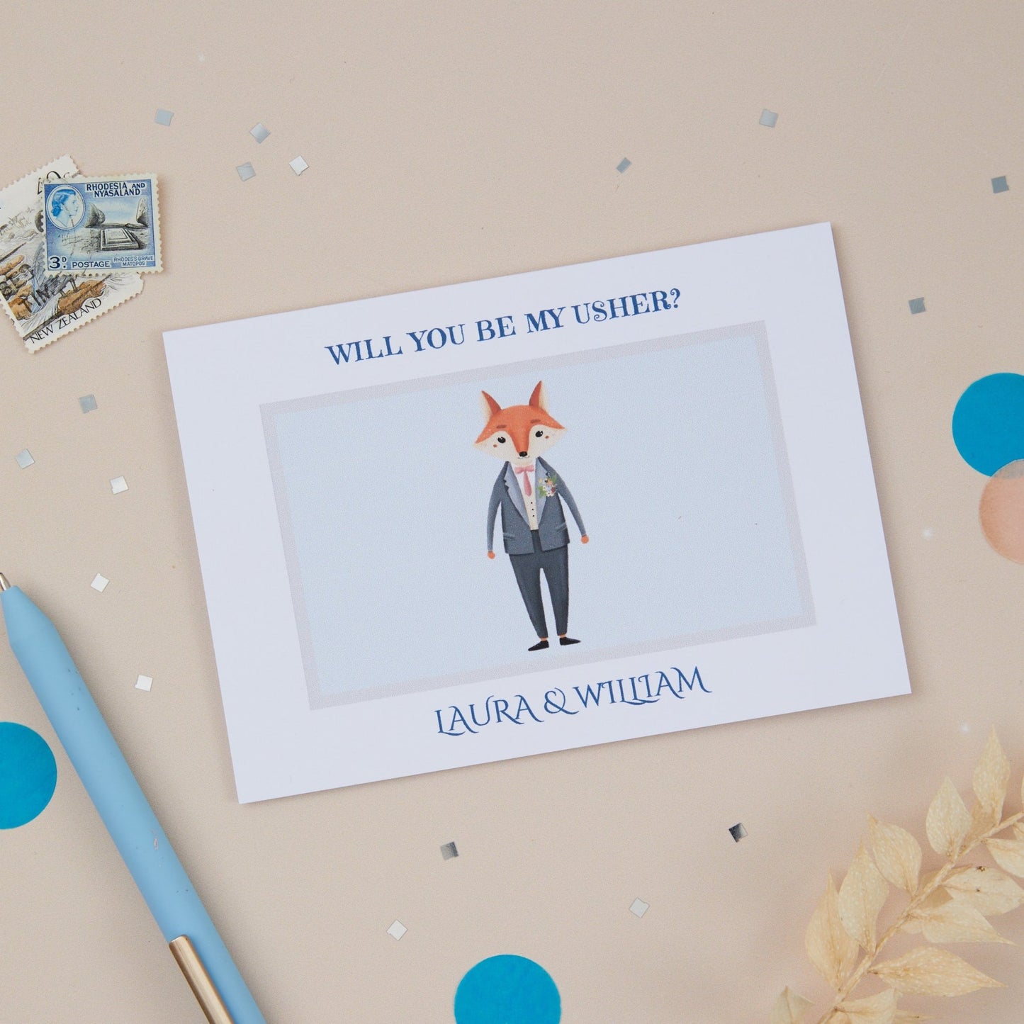 A 'Will You Be My Usher' proposal card with a cartoon fox in a suit illustration, placed on a table with confetti, a pen, and an envelope.