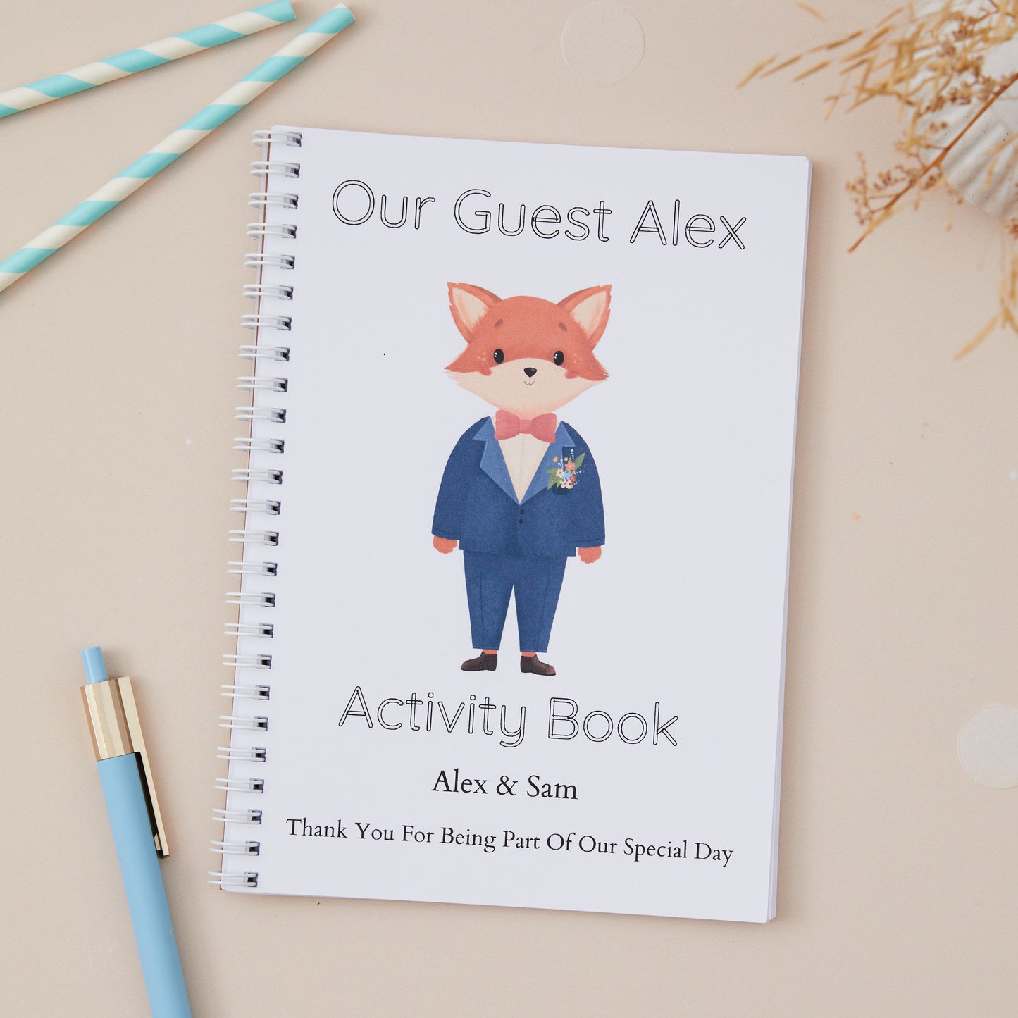 A Blue-Suited Fox Wedding Activity Book Pack For Kids  with a cute fox design, labeled 'Our Guest Alex activity book' with the names of the couple and the label 'thanks for being part of our special day. The activity book is set against a light beige background. There is a Boy Baby Fox in the centre of the book, he is wearing a bow tie and blue suit.