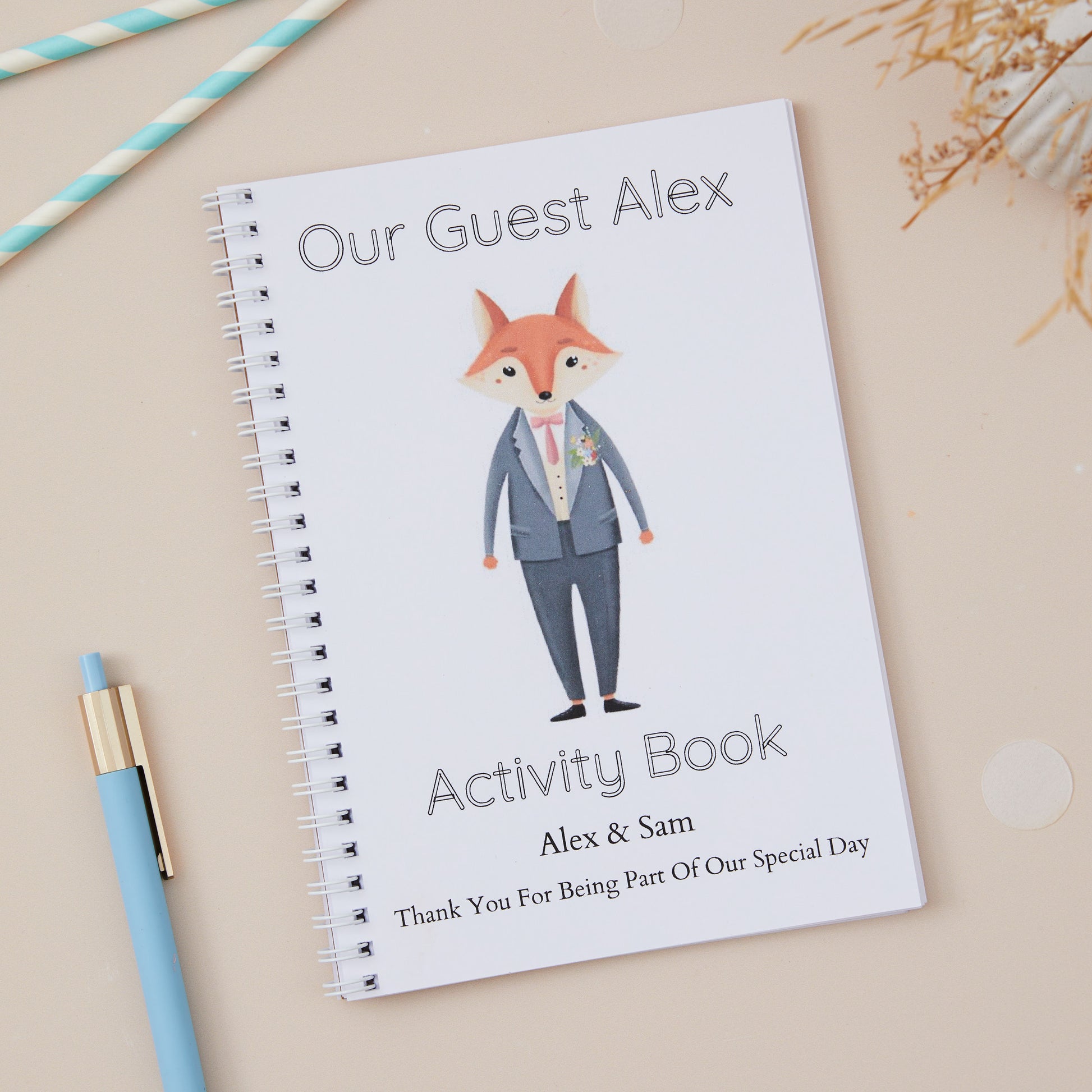 Dapper Grey-Suited Fox Children's Wedding Activity Book Pack 'Our Guest Alex Activity Book' is the text on the front. With a Dapper Grey-Suited Fox character design on the cover, alongside a blue pen and decorative elements. Option to add the name of the couple and their wedding date.