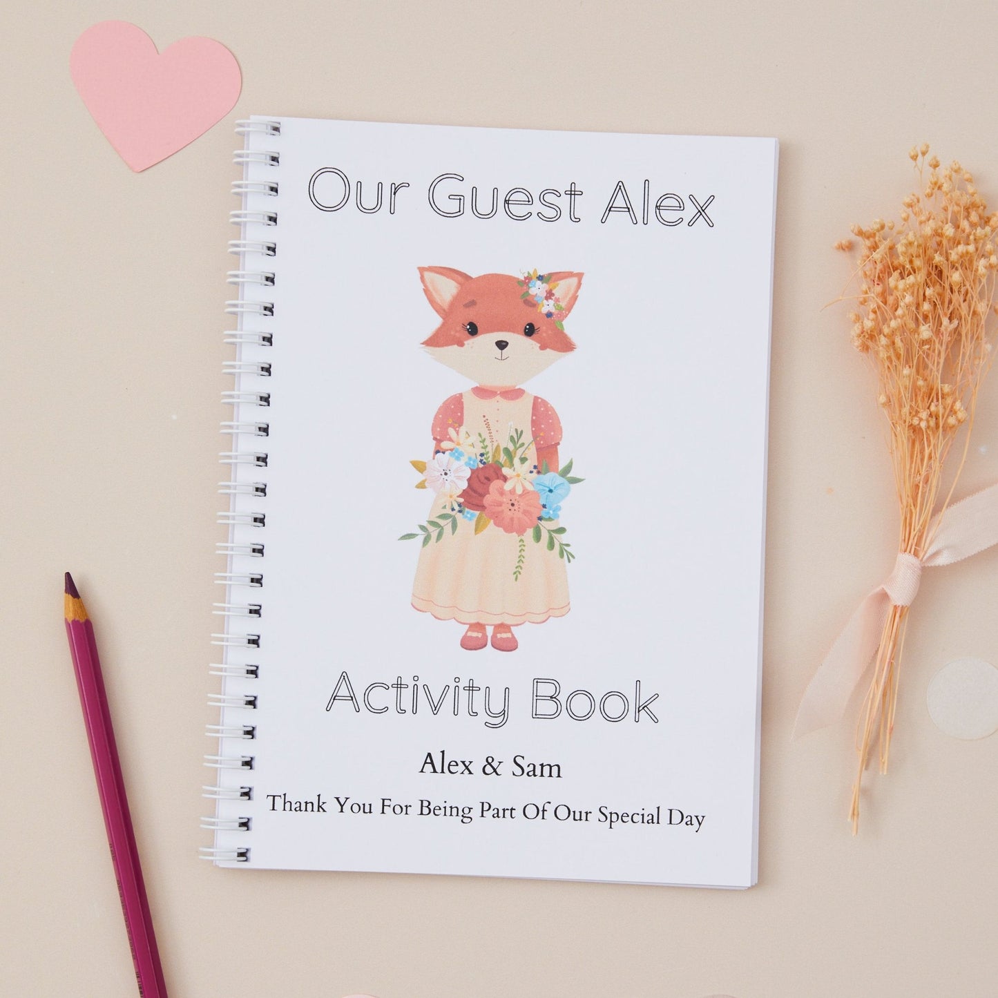 Personalised Little Fox Guest Girl Wedding Activity Book pack for kids  alongside a pen and some dried flowers, on a table with decoration.