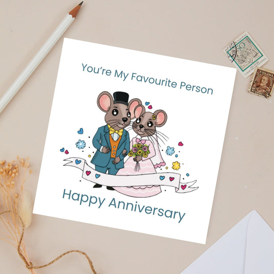 Wedding Anniversary card with cartoon mice couple dressed for their wedding day on a beige surface with stationery items.