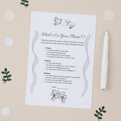 A5 sized game card with the title 'What's On Your Phone?' for wedding reception activities. Guests earn points according to the items on the list which they must have on their phone to win the points. The Card is placed on a table with a pen and decorative elements.